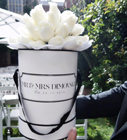 Beautiful large fresh white roses at a wedding ceremony in full bloom in a personalised white hat box with a custom personalised message reading "Mr & Mrs Dimovski Est. 26.11.2016" held by the Groom. Made by Cartel Flowers (the worlds first personalised flowers) You can customise & personalise the writting message on the box with anything, for any occasion. These personalised white roses were used at the wedding ceremony on the signing table and in wedding morning photos at the Bride's house. 